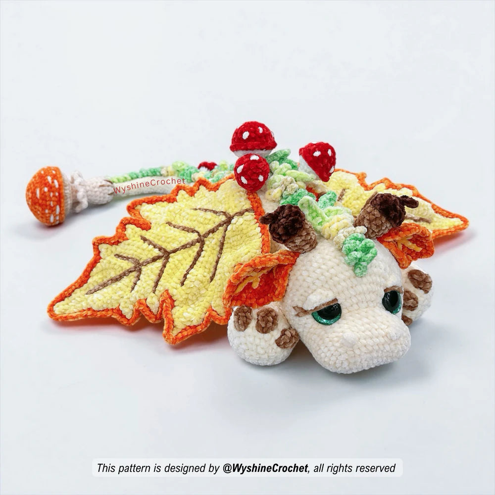 Close-up of Fall Dragon amigurumi plushie with sleepy eyes, acorn horns, orange ears, and soft chenille yarn texture
