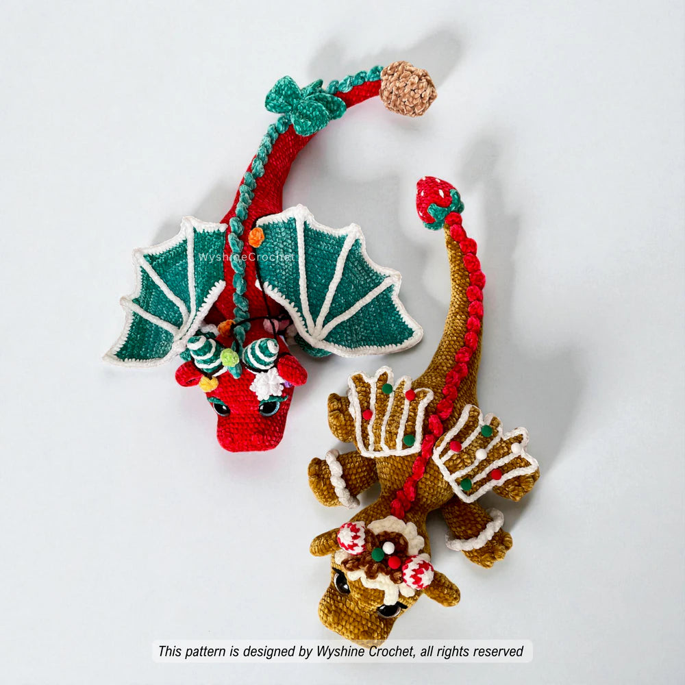 Top view of two Christmas dragon amigurumi designs showing long tails, detailed crochet wings and holiday decorations