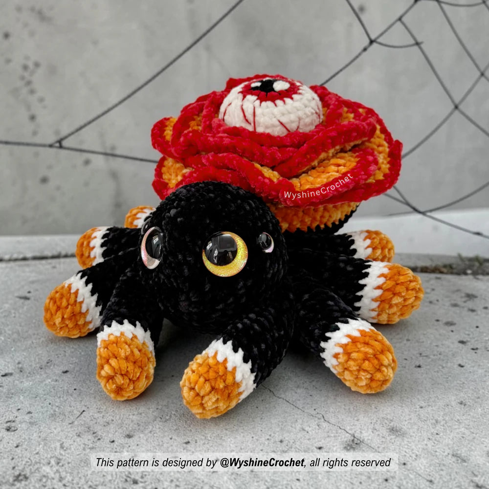 Close-up of Rose Eye Spider crochet plush showing the large central eye, embroidered red veins, layered petals, and soft chenille texture
